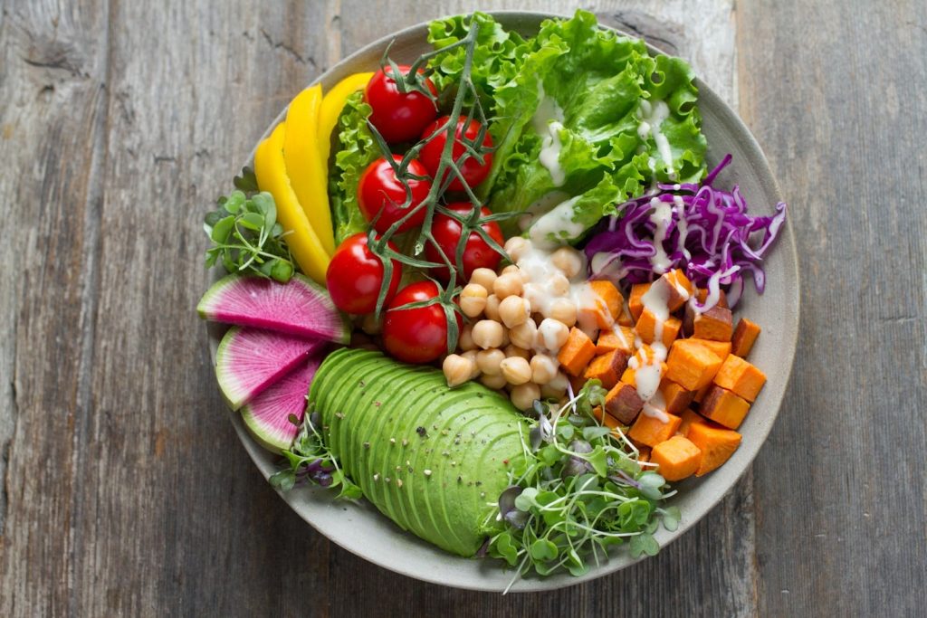 Teller mit Salat, Kichererbsen, Süßkartoffeln, Feigen, Avocado, Paprika, Rotkraut, Tomaten und Kräutern, CHECKUP360